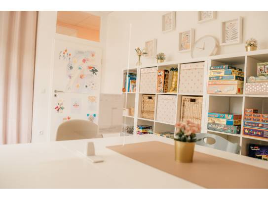 Innenraum mit Regalen voller Spiele, Kinderzeichnungen an der Tür und gemütlicher Einrichtung