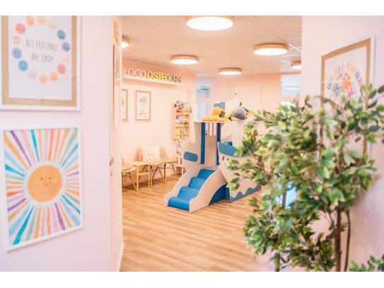 Heller Raum mit Spielschiff, bunten Postern, Pflanzen und Sitzmöglichkeiten für Kinder