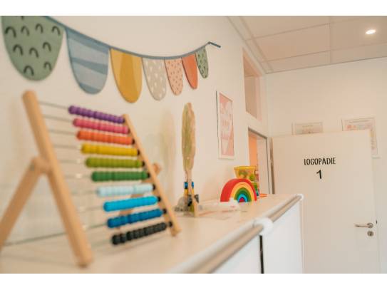 Therapiebereich mit farbenfrohem Spielzeug und Türbeschriftung „Logopädie 1“