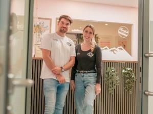 Lukas und Johanna May stehen nebeneinander im Eingangsbereich einer modern gestalteten Praxis.
