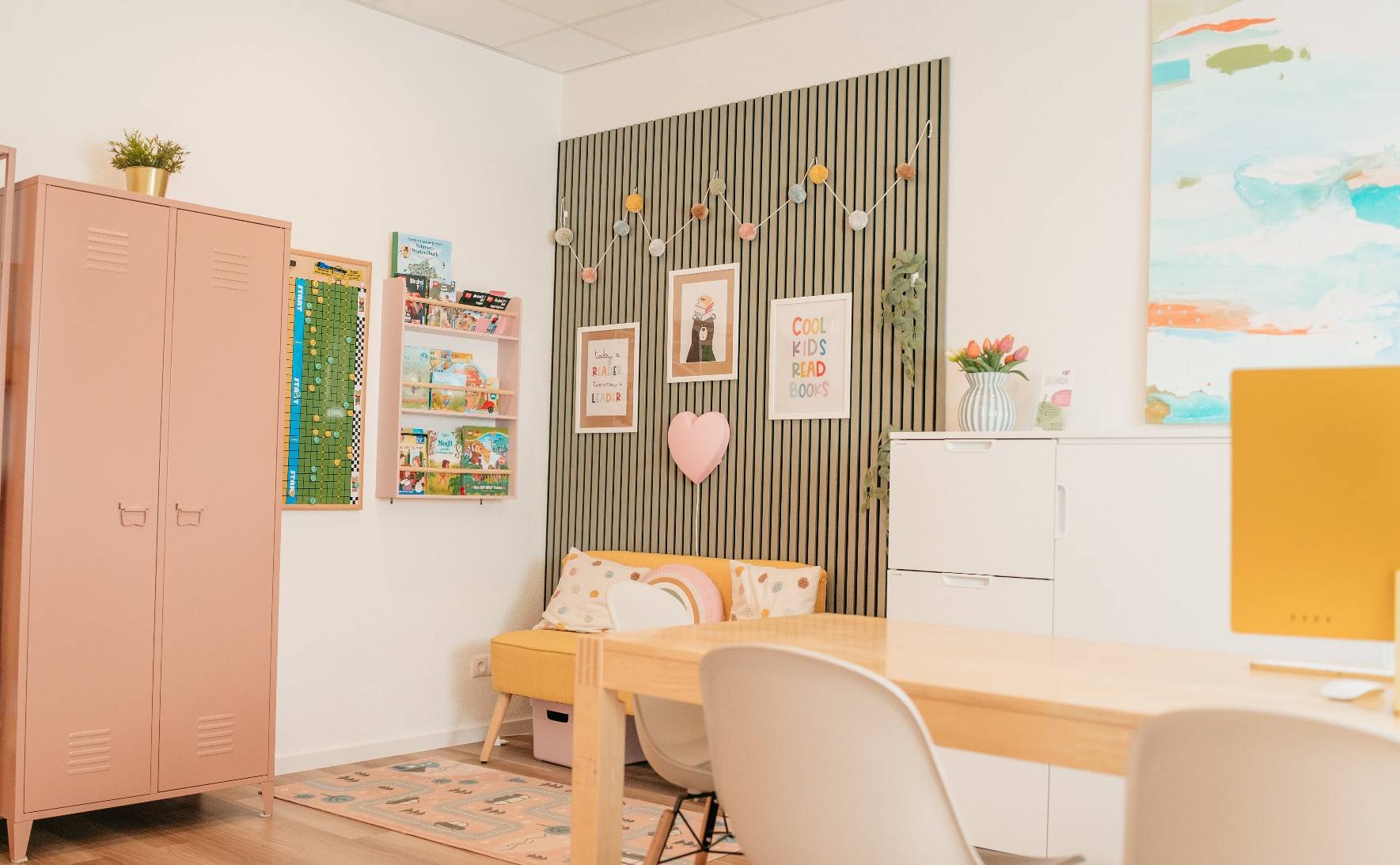 Innenraum mit Regal, Tisch, Kinderecke und farbiger Wandgestaltung, ausgestattet mit Spielen und Büchern