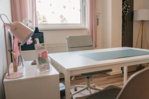 Ordentlich eingerichtetes Büro mit Schreibtisch und Stuhl, Fenster mit Blumenaufklebern im Hintergrund