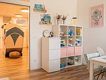 Heller Raum mit Regal voller Spiele und Bücher, Blick in angrenzenden Spielbereich mit großem Spielgerät