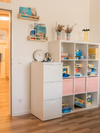 Heller Raum mit Regal voller Spiele und Bücher, Blick in angrenzenden Spielbereich mit großem Spielgerät