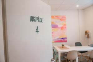 Geöffnete Tür mit der Aufschrift „Logopädie 4“, dahinter ein heller Therapieraum mit buntem Wandbild und freundlicher Einrichtung