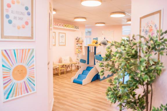 Heller Raum mit Spielschiff, bunten Postern, Pflanzen und Sitzmöglichkeiten für Kinder