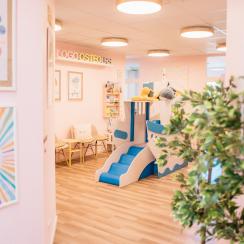 Heller Raum mit Spielschiff, bunten Postern, Pflanzen und Sitzmöglichkeiten für Kinder