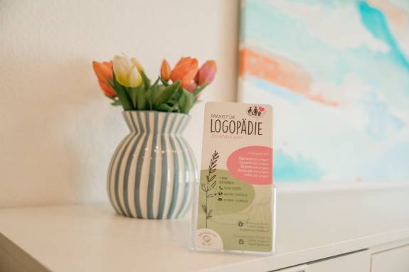 Flyerhalter mit Logopädie-Flyer auf weißem Schrank neben einer Vase mit Tulpen